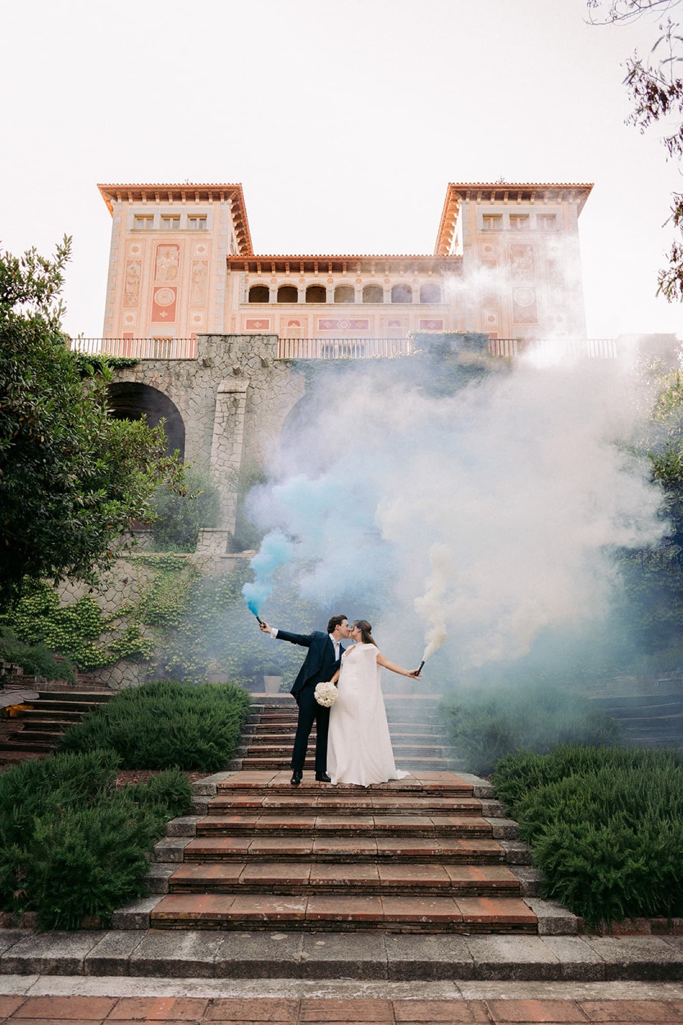 Novios en la escalinata de un palacio entre bengalas de humo