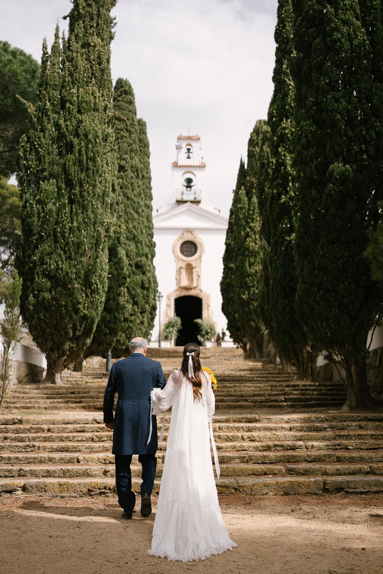 Novia subiendo entre cipreses hacia la iglesia el día de su boda