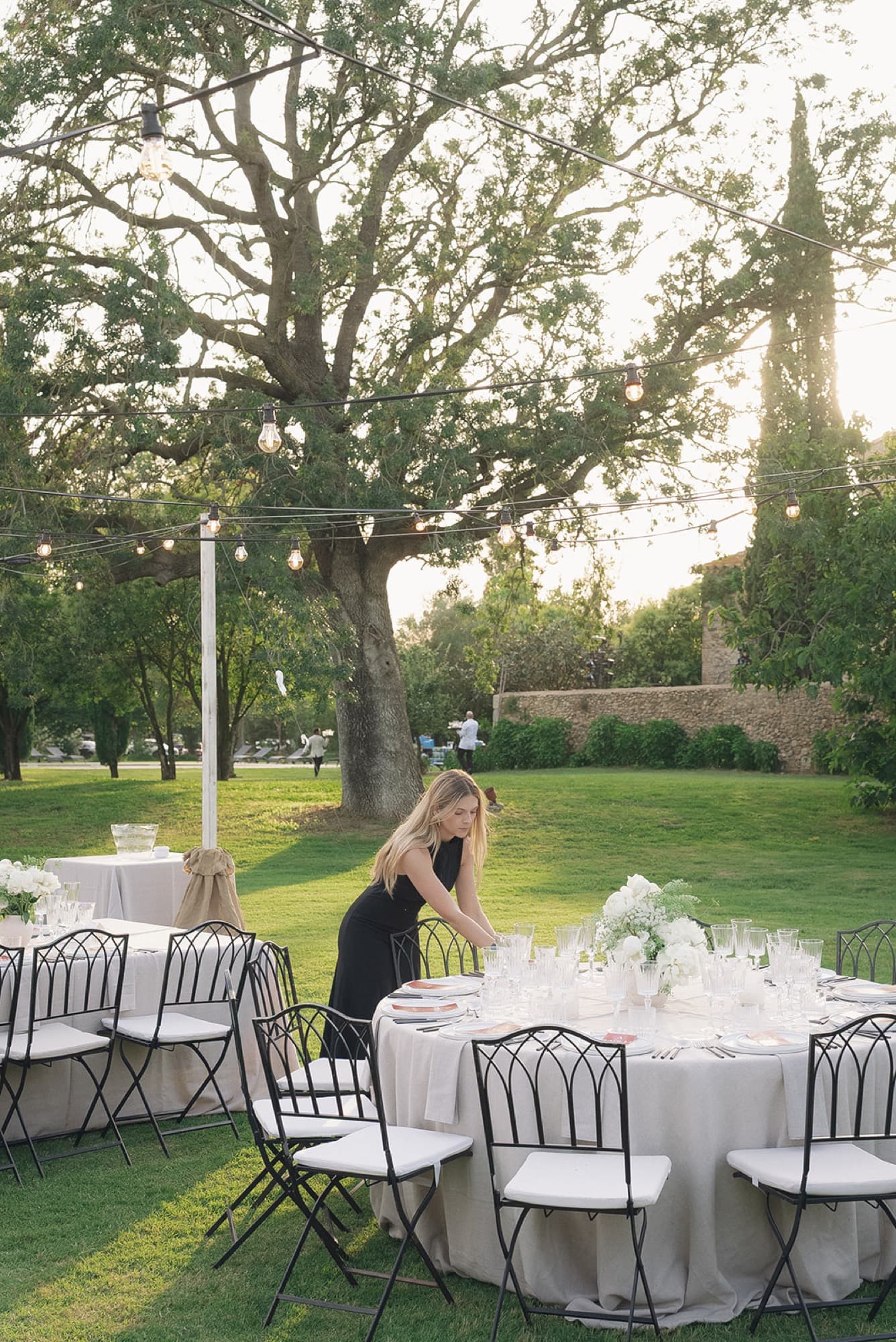 Elisenda Herrero montando una mesa redonda en el jardín, al atardecer, bajo guirnaldas de luces